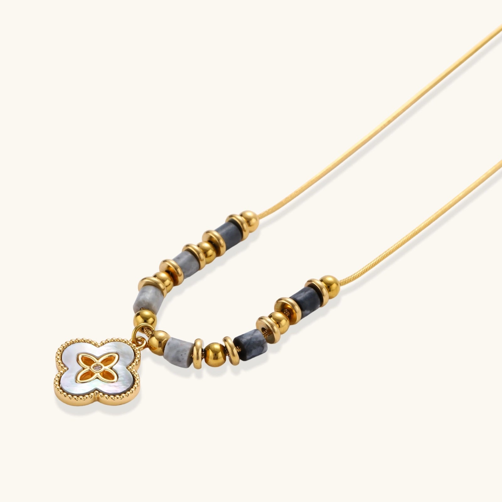 Close-up of iridescent abalone clover pendant with zircon center and grey gemstone beads in 18K gold