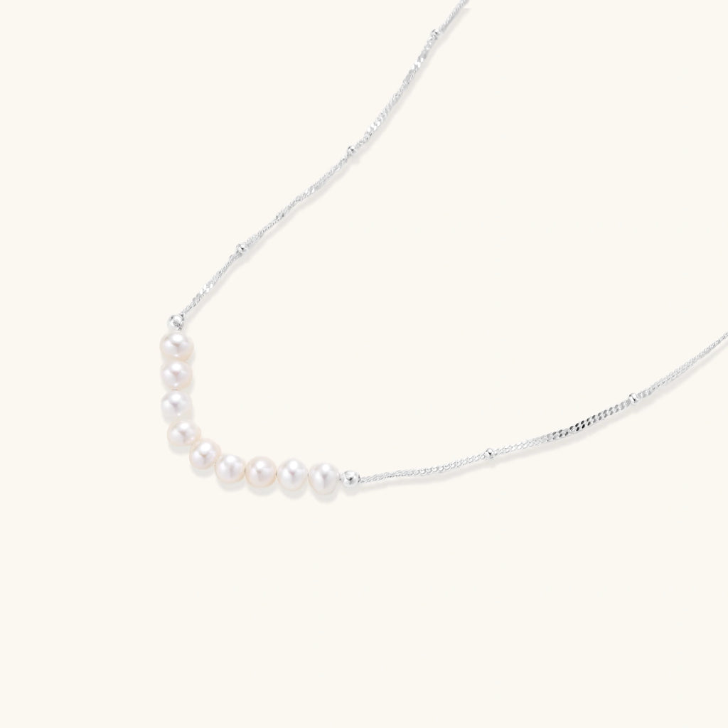 Close-up of nine freshwater pearls aligned in a dainty crescent on rhodium-plated 925 silver chain by VAHN Jewels