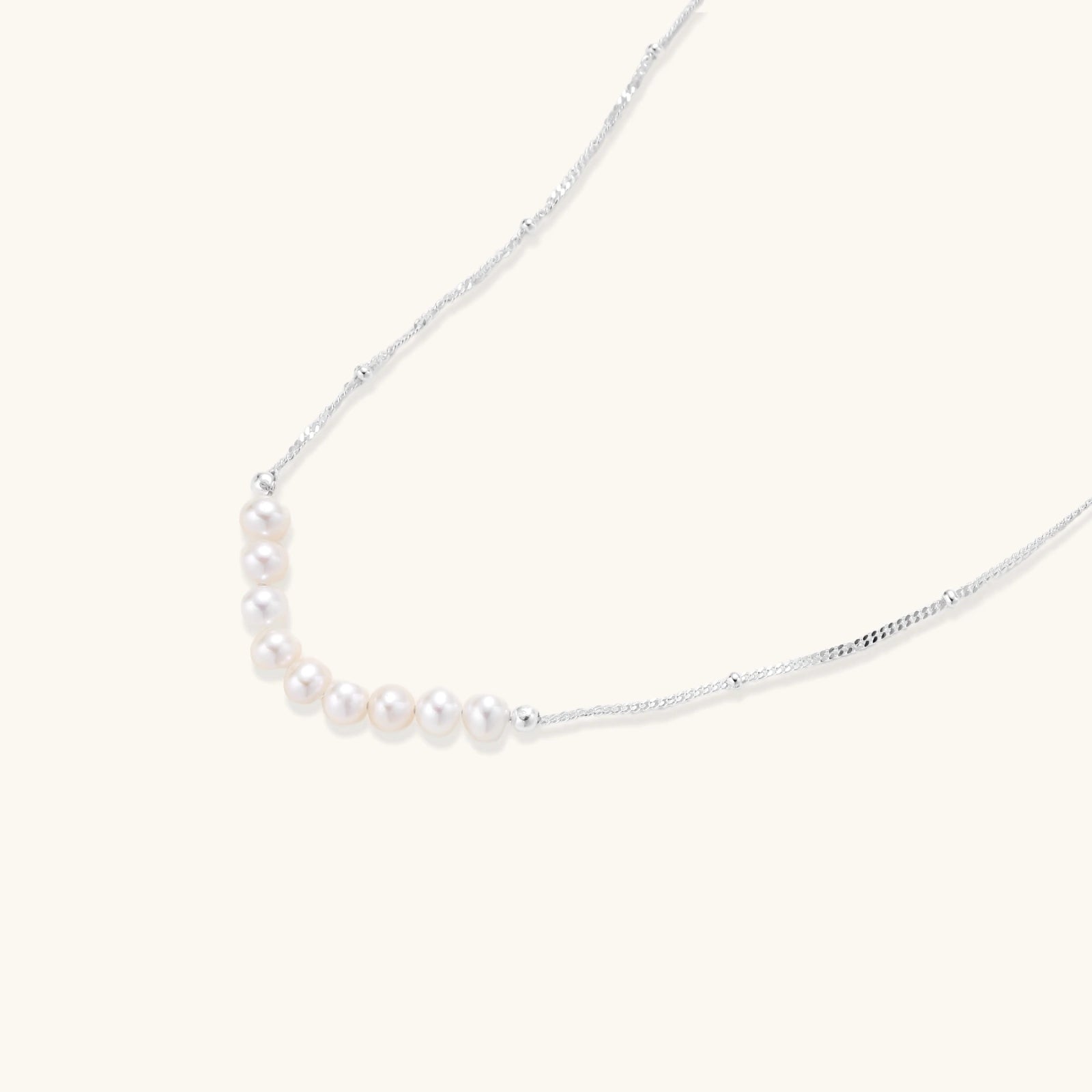 Close-up of nine freshwater pearls aligned in a dainty crescent on rhodium-plated 925 silver chain by VAHN Jewels