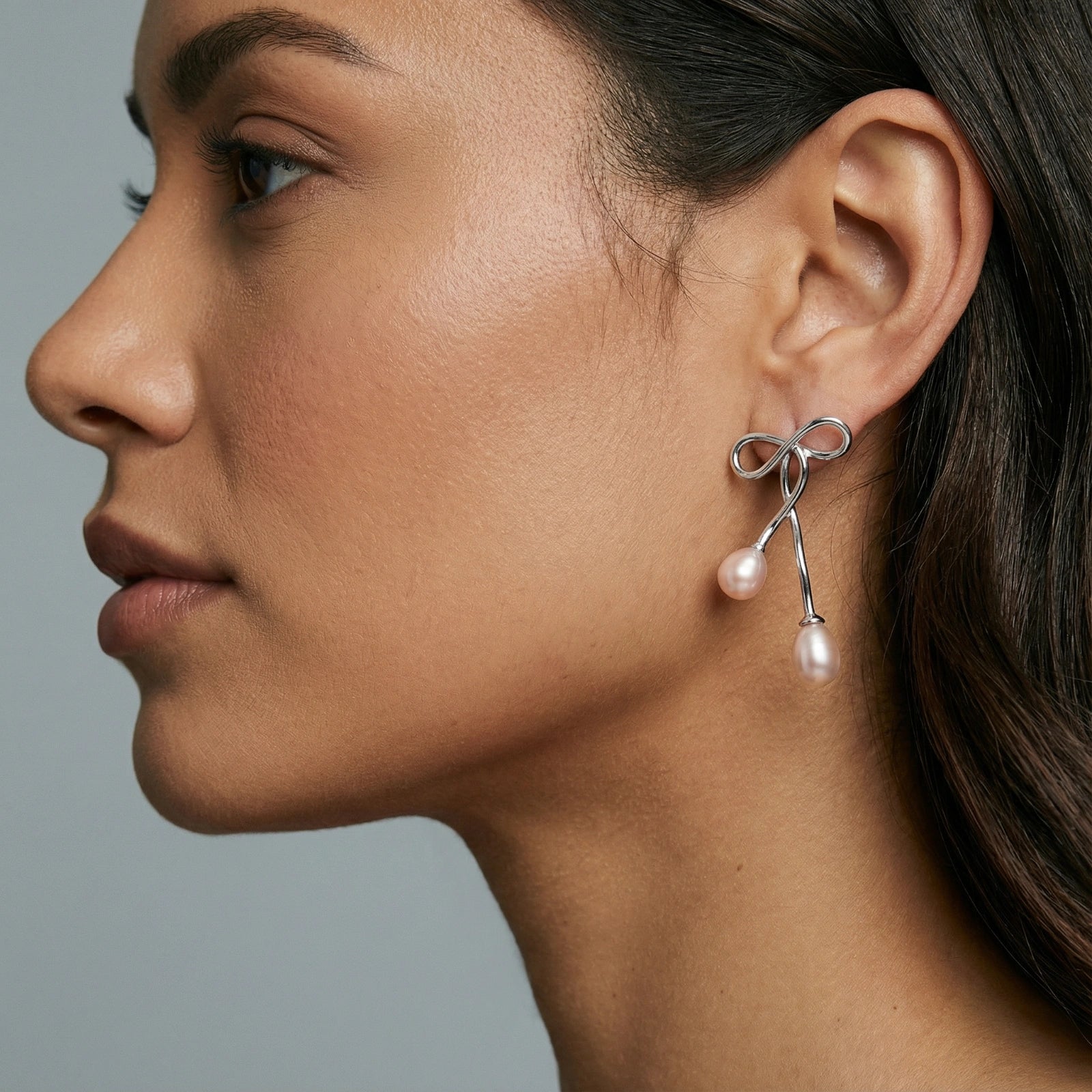 Woman wearing silver bow pearl drop earrings in rhodium-plated 925 sterling silver by VAHN Jewels
