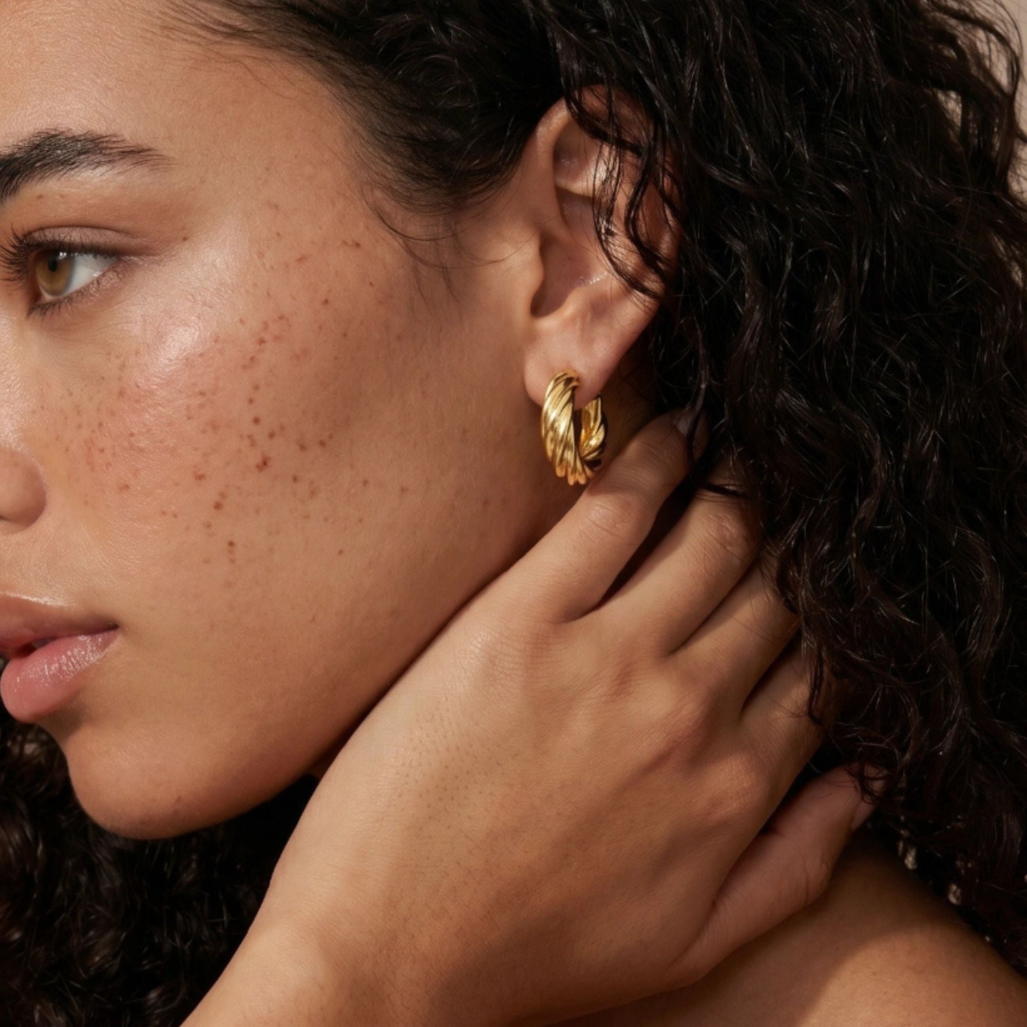 Woman wearing twisted rope gold huggie earrings in 14K gold-plated 925 sterling silver by VAHN Jewels