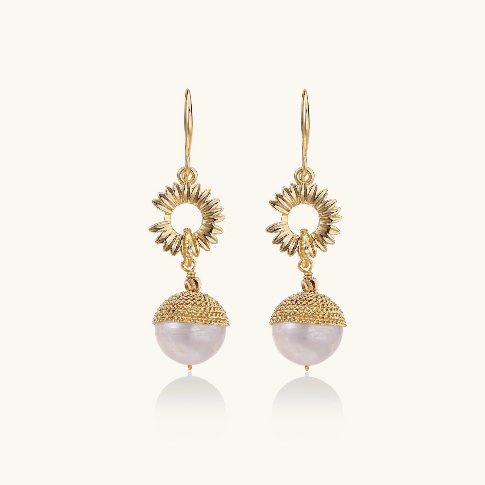 Close-up of gold sunburst charm earrings with baroque pearl — dangle jewelry